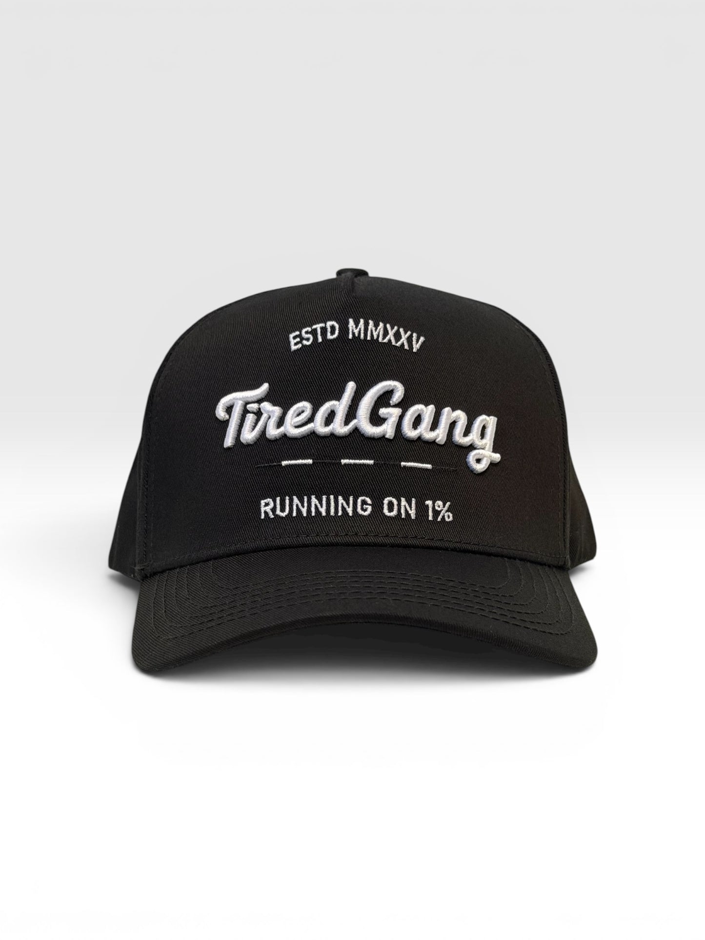 Black five panel cap with the text 'ESTD MMXXV Tired Gang running on 1%' embroidered on a white background